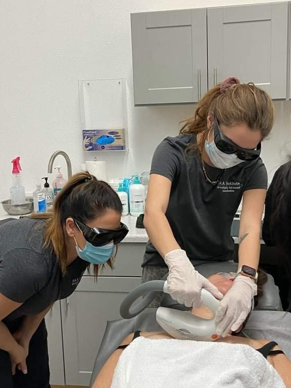 An instructor in laser safety eyewear supervising a student's treatment on a model